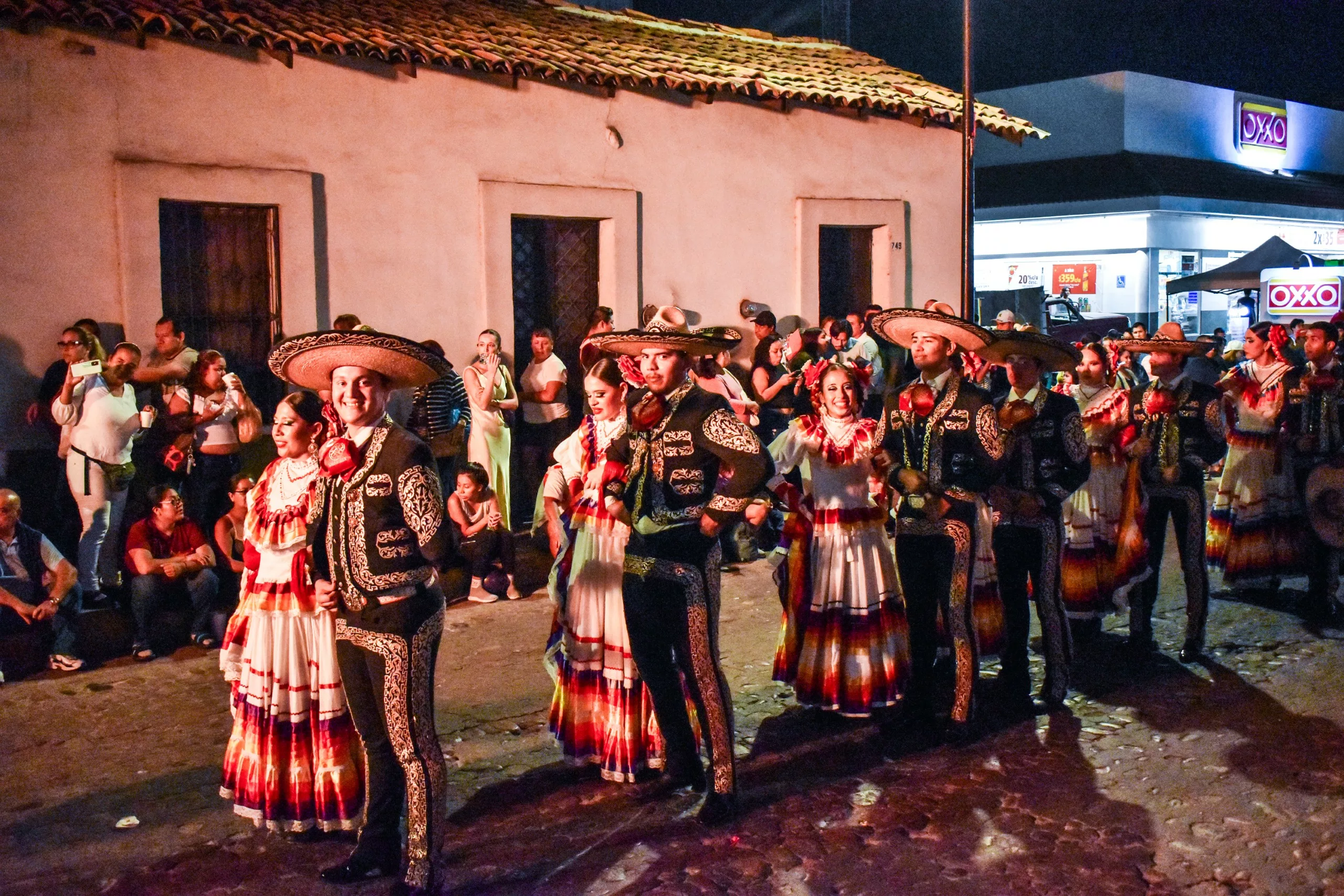 Un groupe vêtu de costumes traditionnels de mariachi se tient dans une rue pavée, la nuit venue