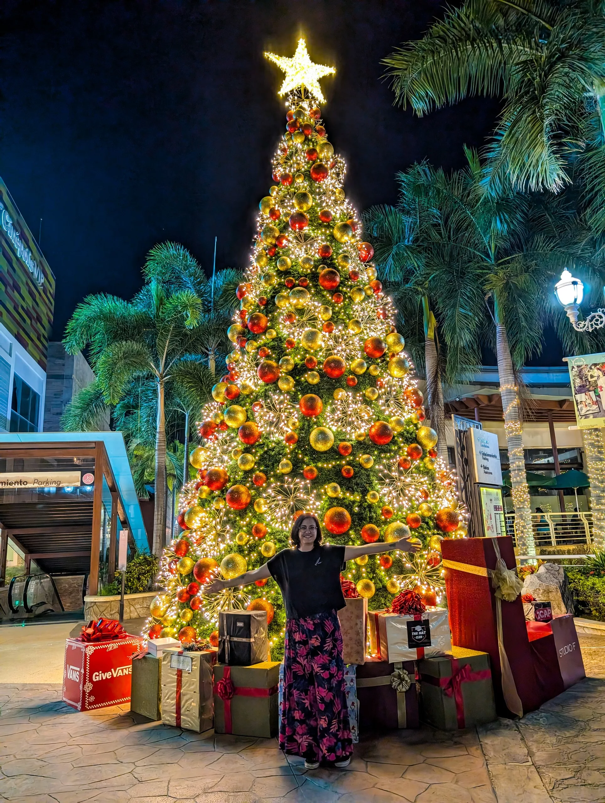 Un grand sapin de noël décoré et illuminé avec une personne en t-shirt au premier plan