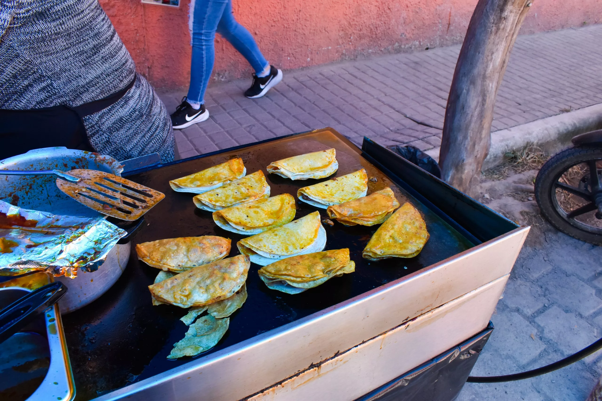 À Mexique, un vendeur ambulant prépare des tortillas pliées sur une plaque chauffante, avec une casserole et une spatule à portée de main.