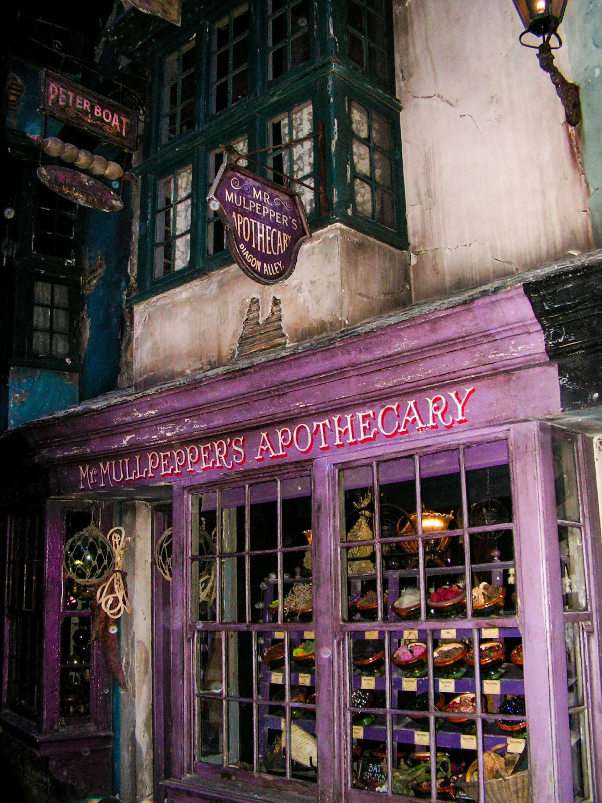 La devanture peinte en violet de l'apothicairerie de M. Mullpepper, située dans le monde de Harry Potter, dans le Chemin de Traverse, avec une vitrine remplie de divers bocaux et récipients.