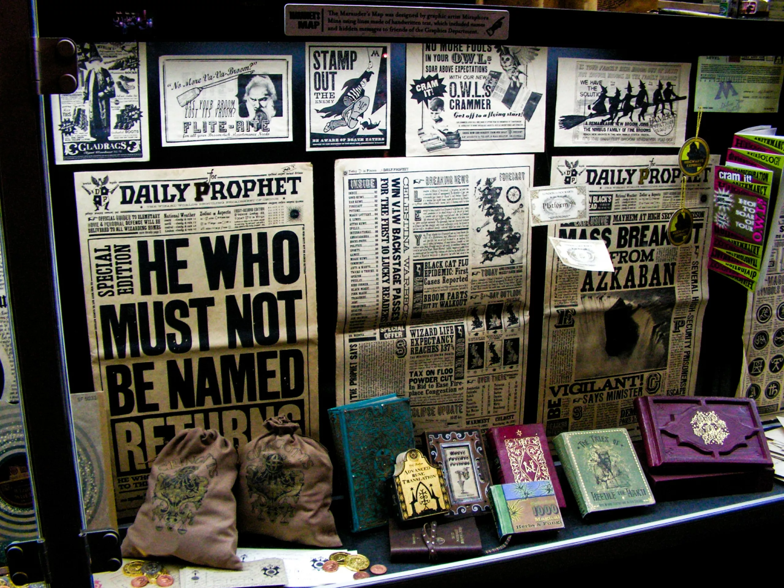 Une vitrine présente des accessoires du Monde des Sorciers de Harry Potter notamment des exemplaires du « Prophète » avec des gros titres consacrés à Voldemort et Sirius Black, divers petits livres, ainsi que deux pochettes à cordon imprimées.