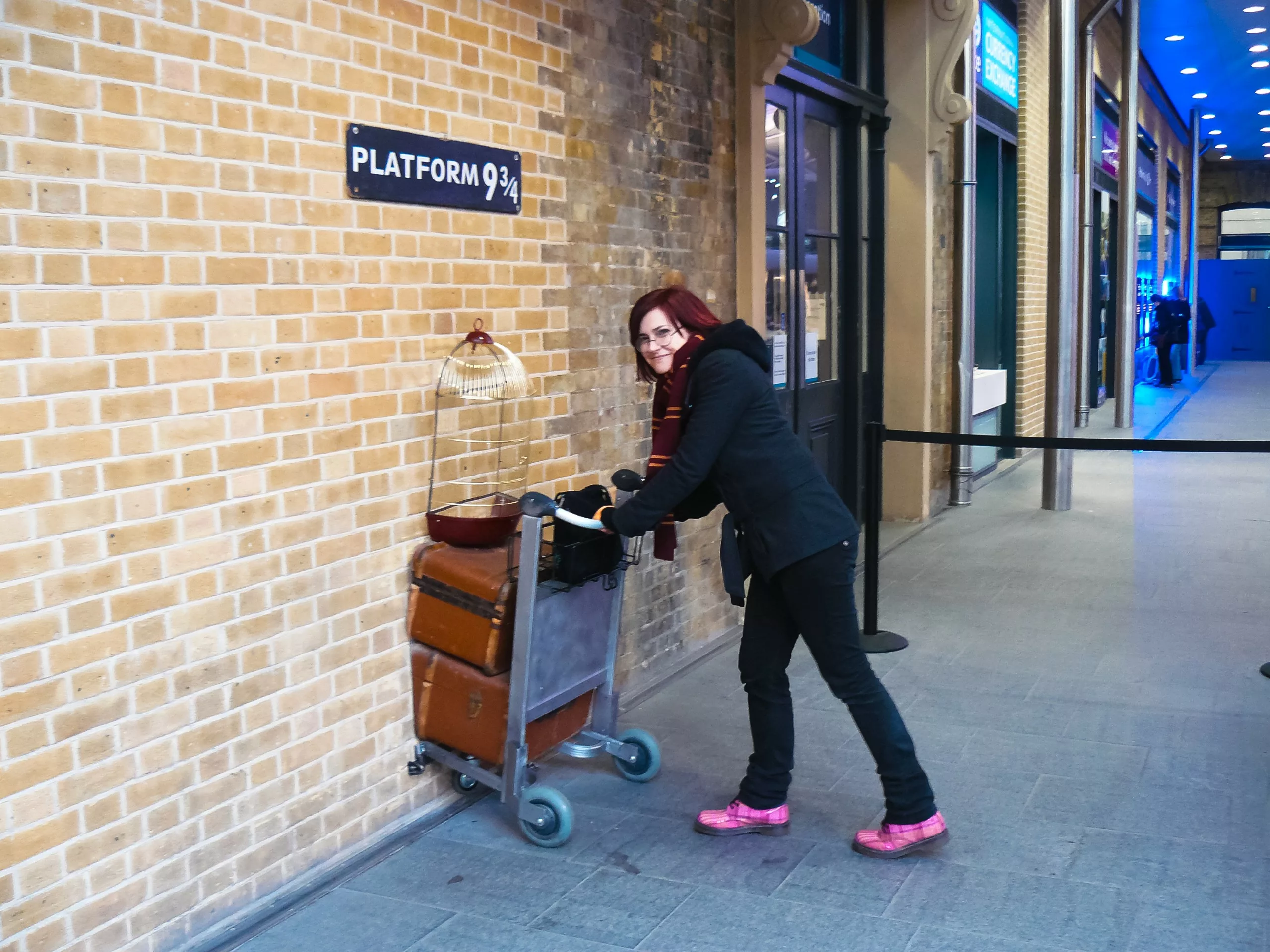 Une personne pousse un chariot à bagages contre un mur de briques sur lequel est apposé un panneau « Quai 9 3/4 » à la gare de King's Cross, un lieu emblématique pour les fans d'Harry Potter en Angleterre