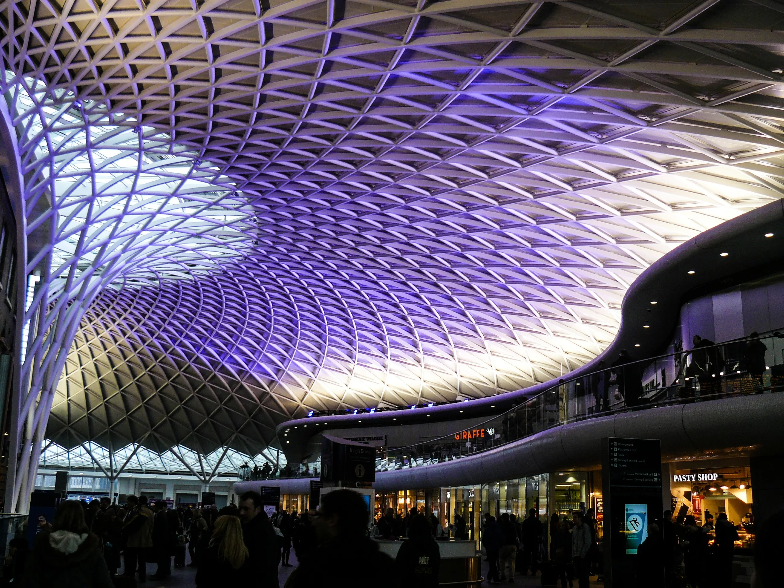 Le plafond voûté en treillis de la gare de King's Cross, emblématique pour les fans d'Harry Potter, est éclairé d'une lumière violette au-dessus du hall et des boutiques du terminal.