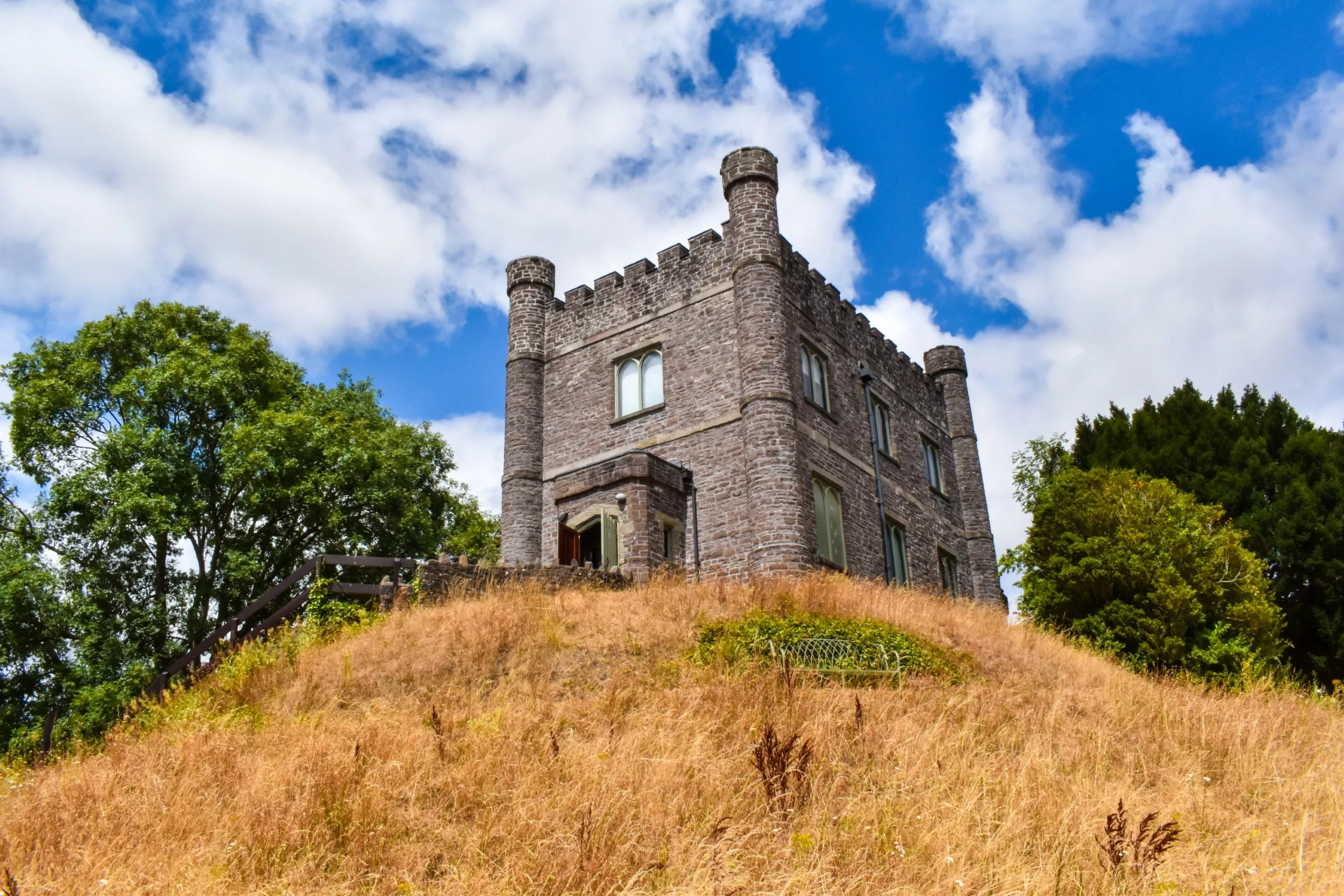 Un château en pierre doté de tourelles se dresse au sommet d'une colline jaune, sous un ciel bleu parsemé de nuages blancs