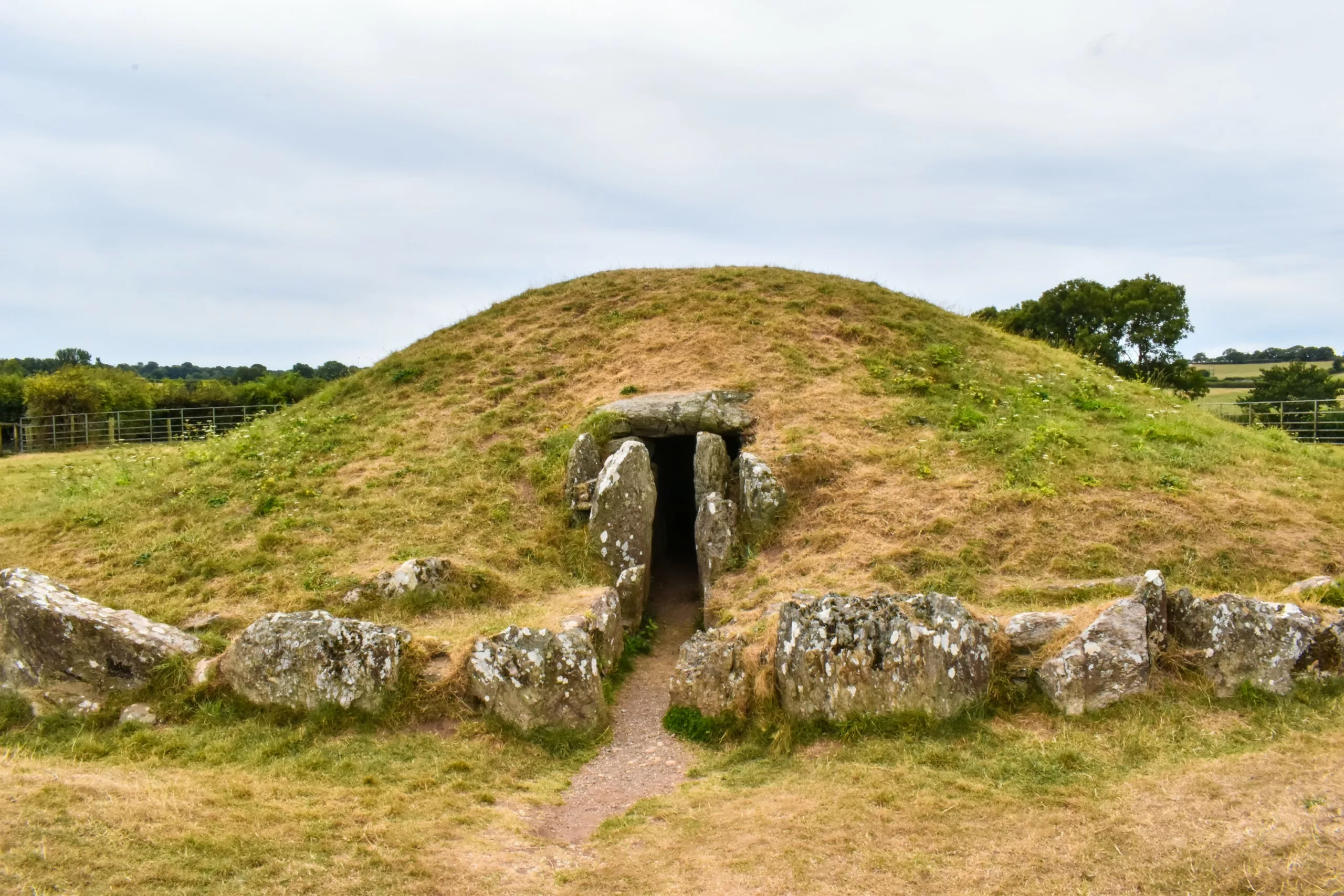 Une chambre funéraire en pierre encastrée dans un tumulus recouvert d'herbe, dotée d'une entrée étroite.