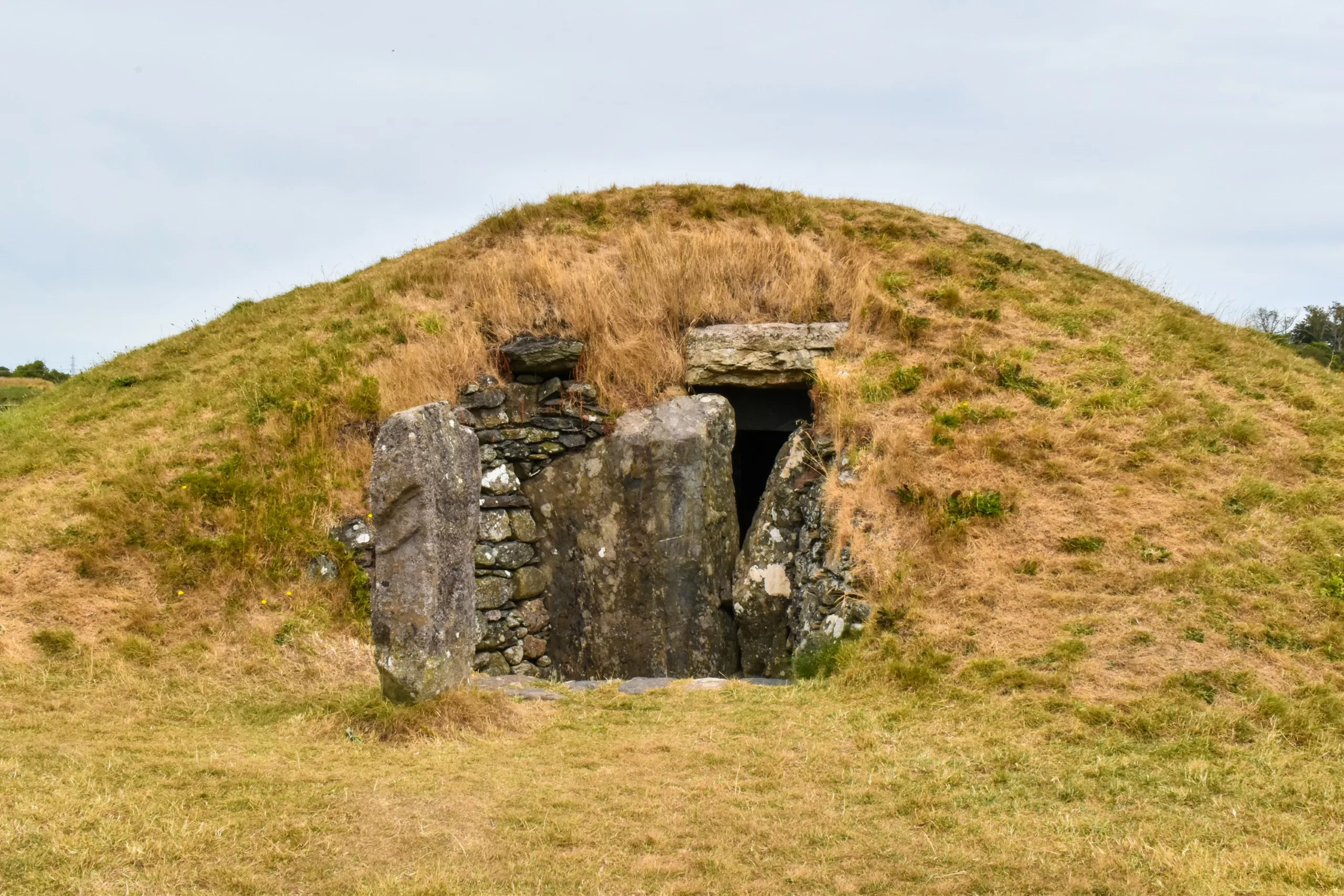 Un tumulus recouvert d'herbe doté d'une entrée bordée de pierres menant à une chambre obscure.