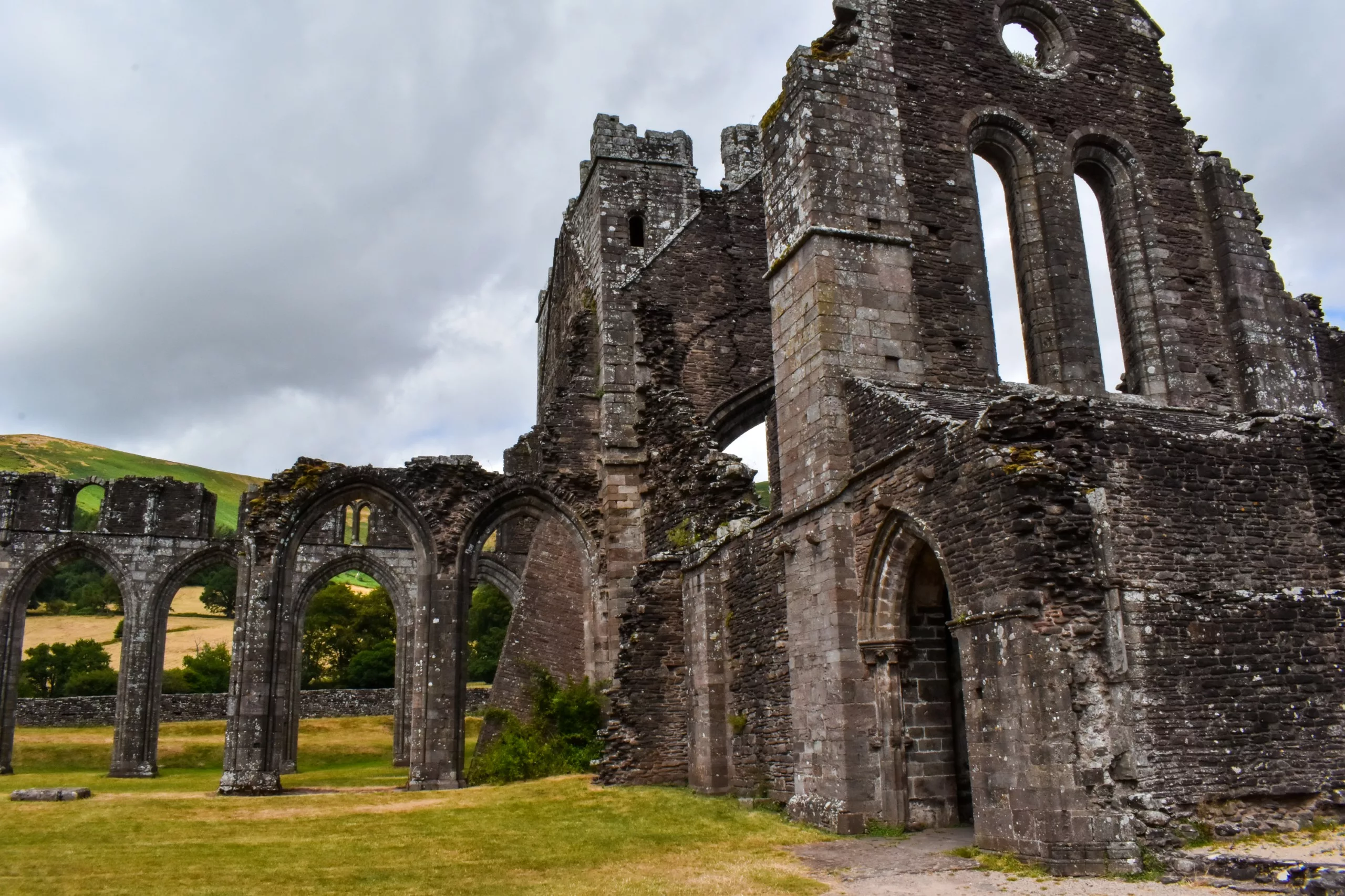 Les ruines en pierre d'une abbaye médiévale au Pays de Galles se caractérisent par de hautes fenêtres cintrées et une structure sans toit nichée au milieu d'un champ.