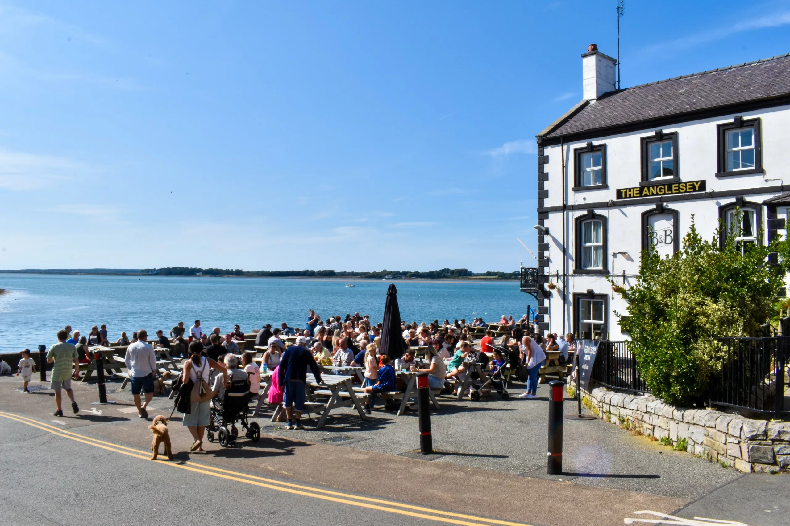 Les clients profitent d'une journée ensoleillée aux tables de pique-nique en plein air du pub « The Anglesey », qui surplombe une baie.