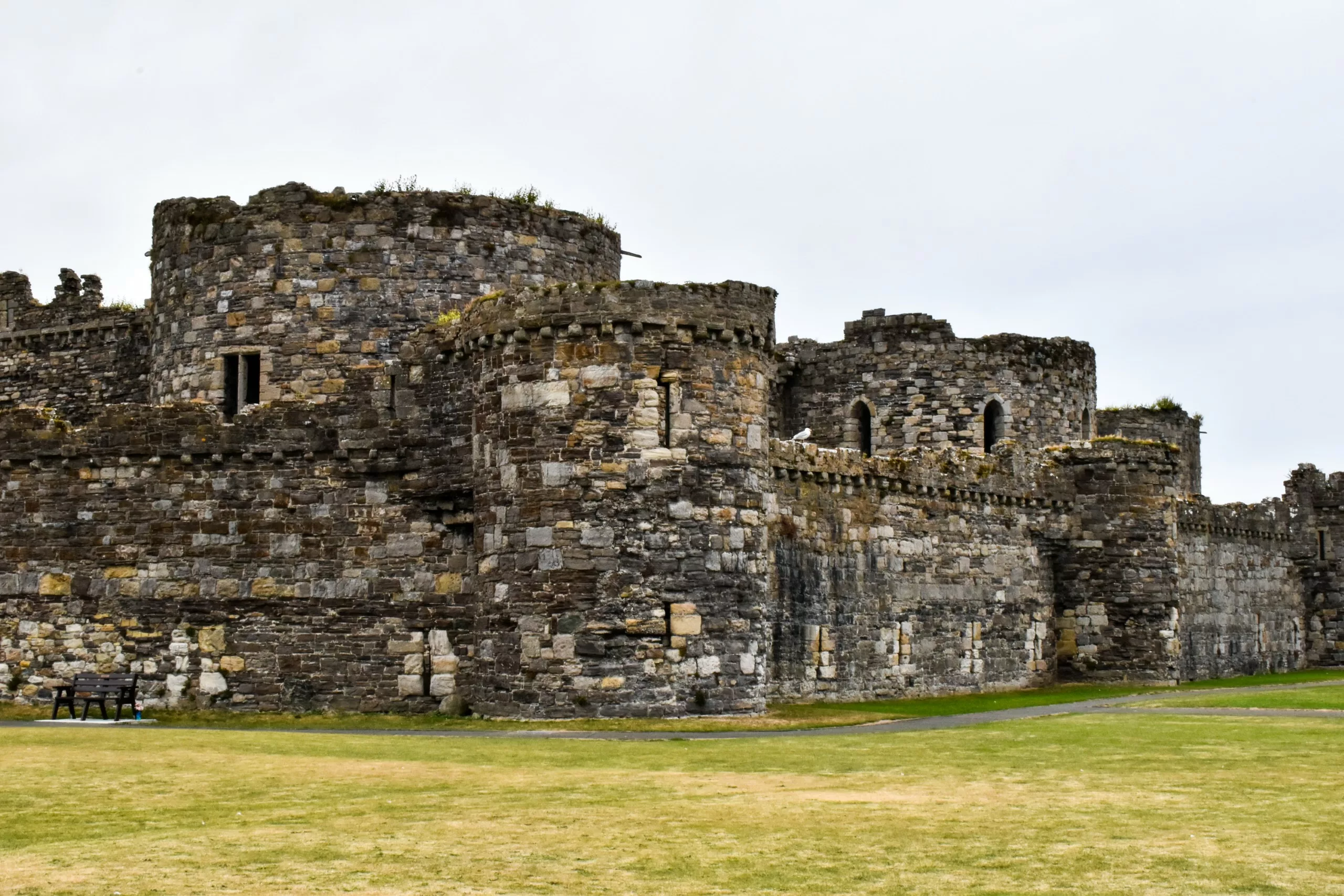 Vue panoramique sur les ruines d'un petit château en pierre au Pays de Galles, avec ses tours circulaires et ses remparts, se détachant sur une pelouse.
