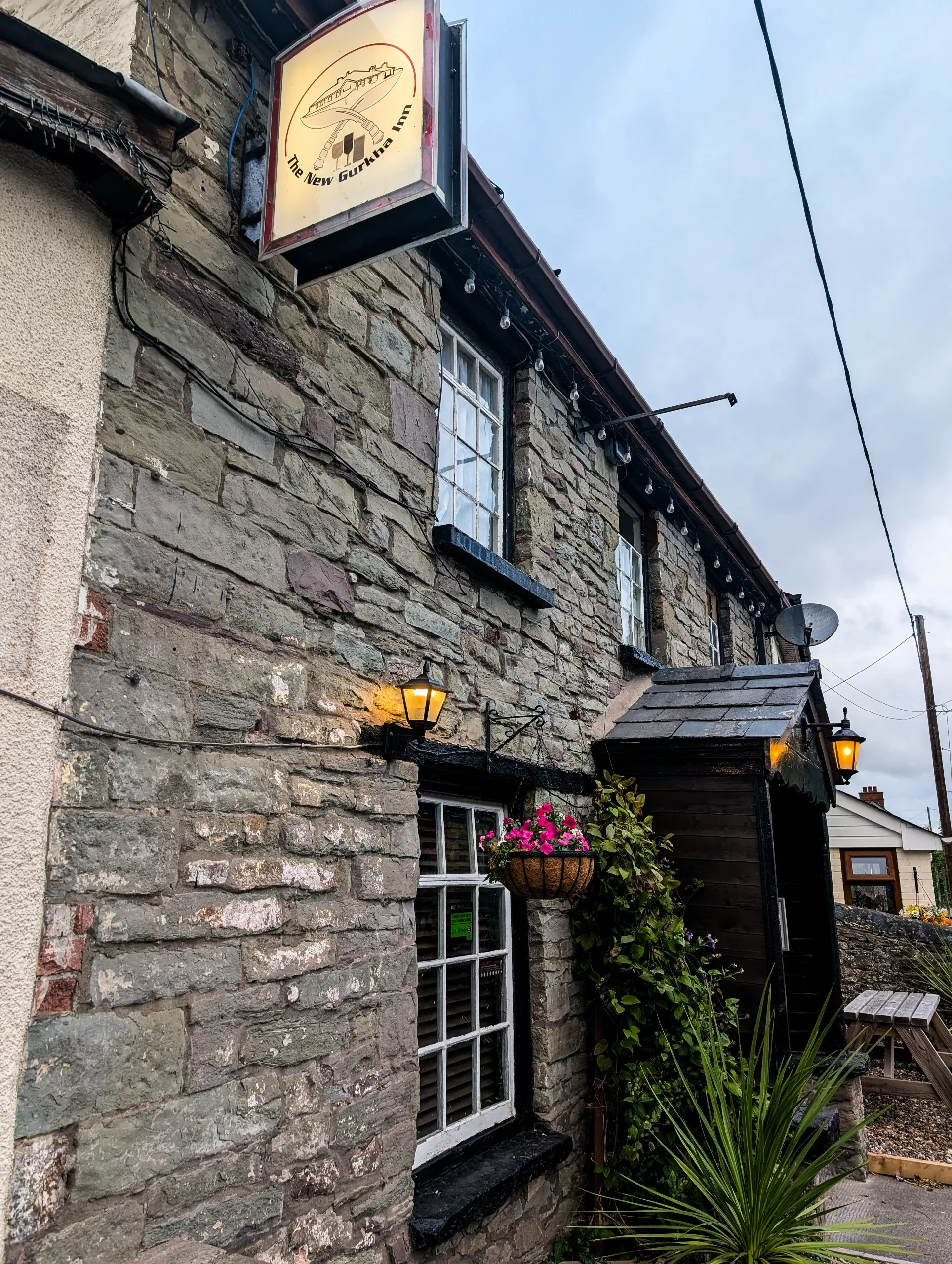 Façade en pierre du « New Gurkha Inn », un restaurant à découvrir au Pays de Galles, avec son enseigne suspendue, ses petites fenêtres et son porche d’entrée en bois.
