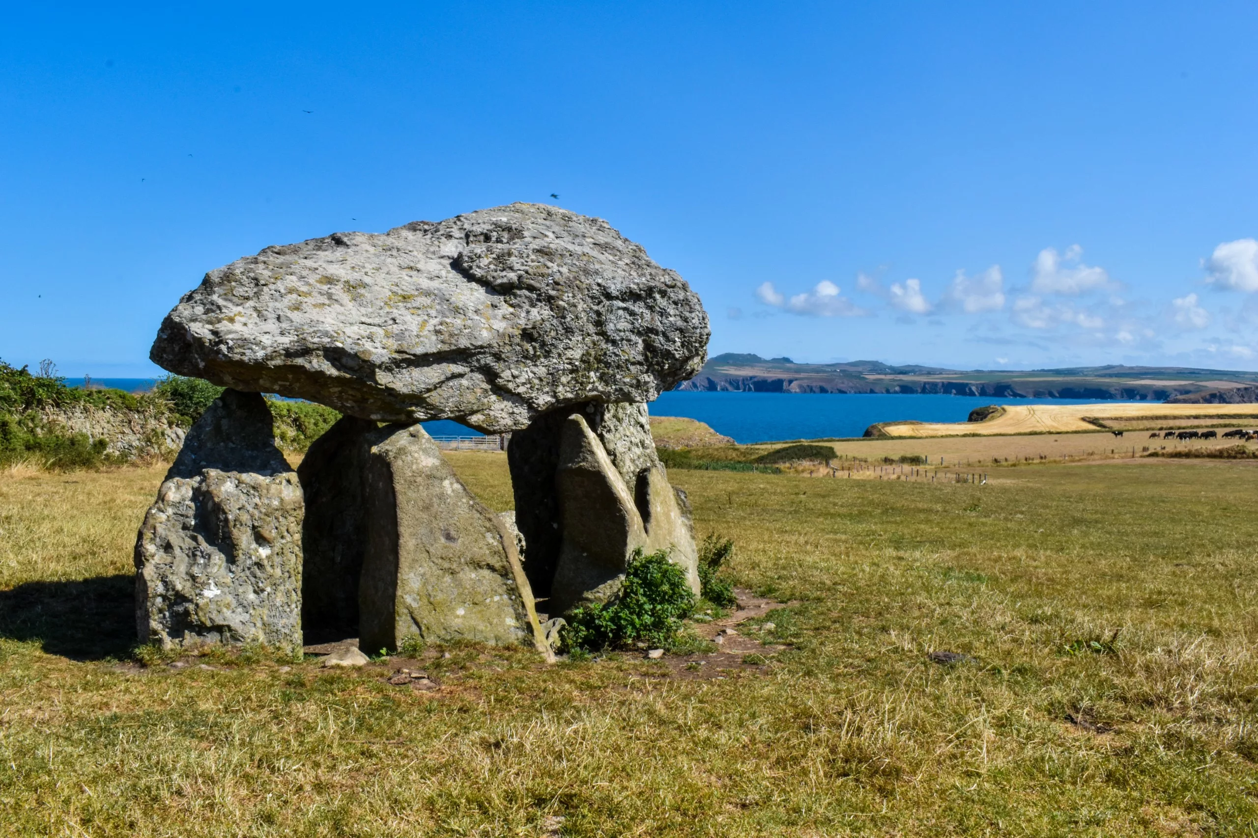 Un dolmen préhistorique en pierre se dresse dans un champ verdoyant surplombant une baie côtière du Pays de Galles.