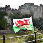Le drapeau du Pays de Galles flotte devant un château en pierre et une rivière