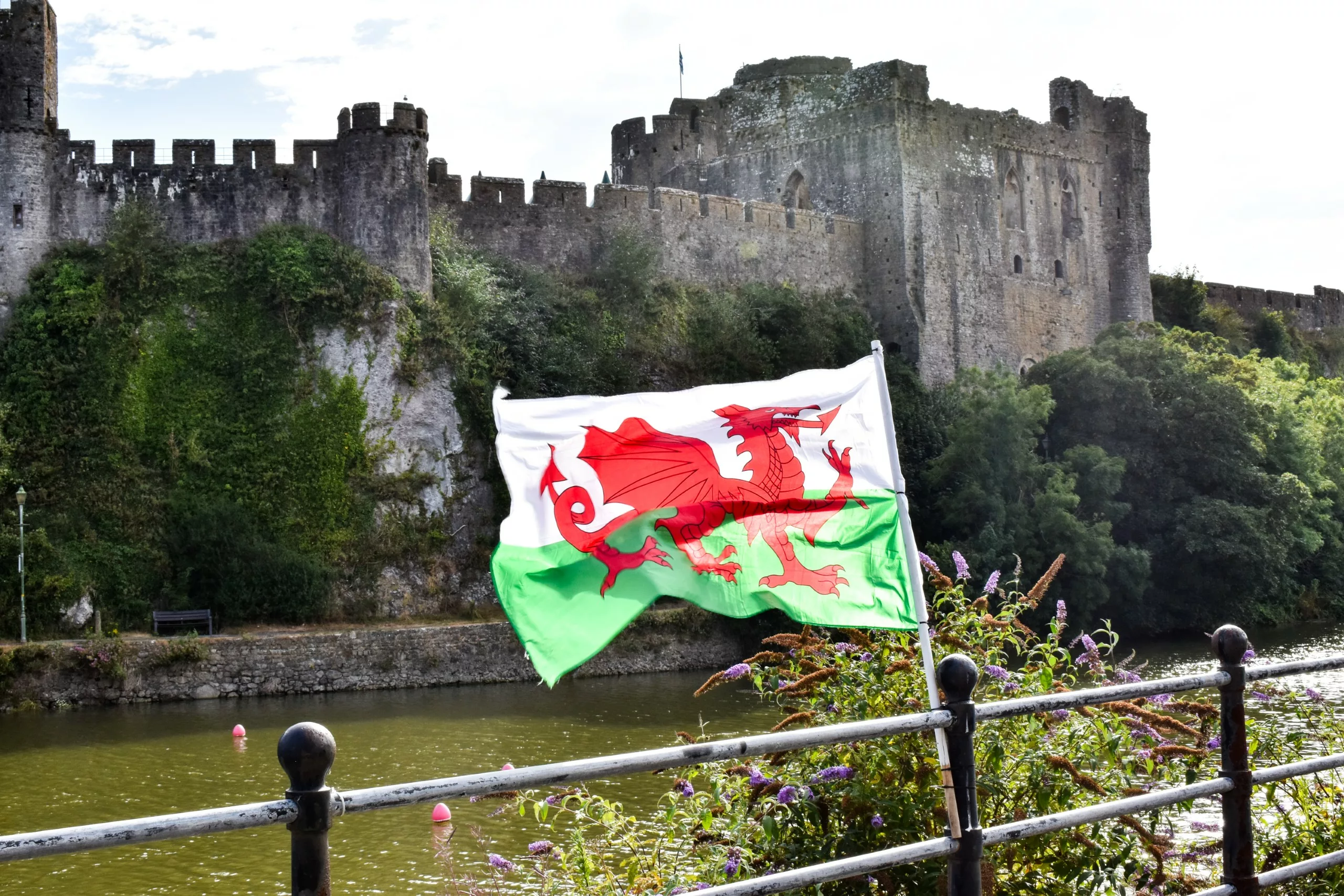 Le drapeau du Pays de Galles flotte devant un château en pierre et une rivière