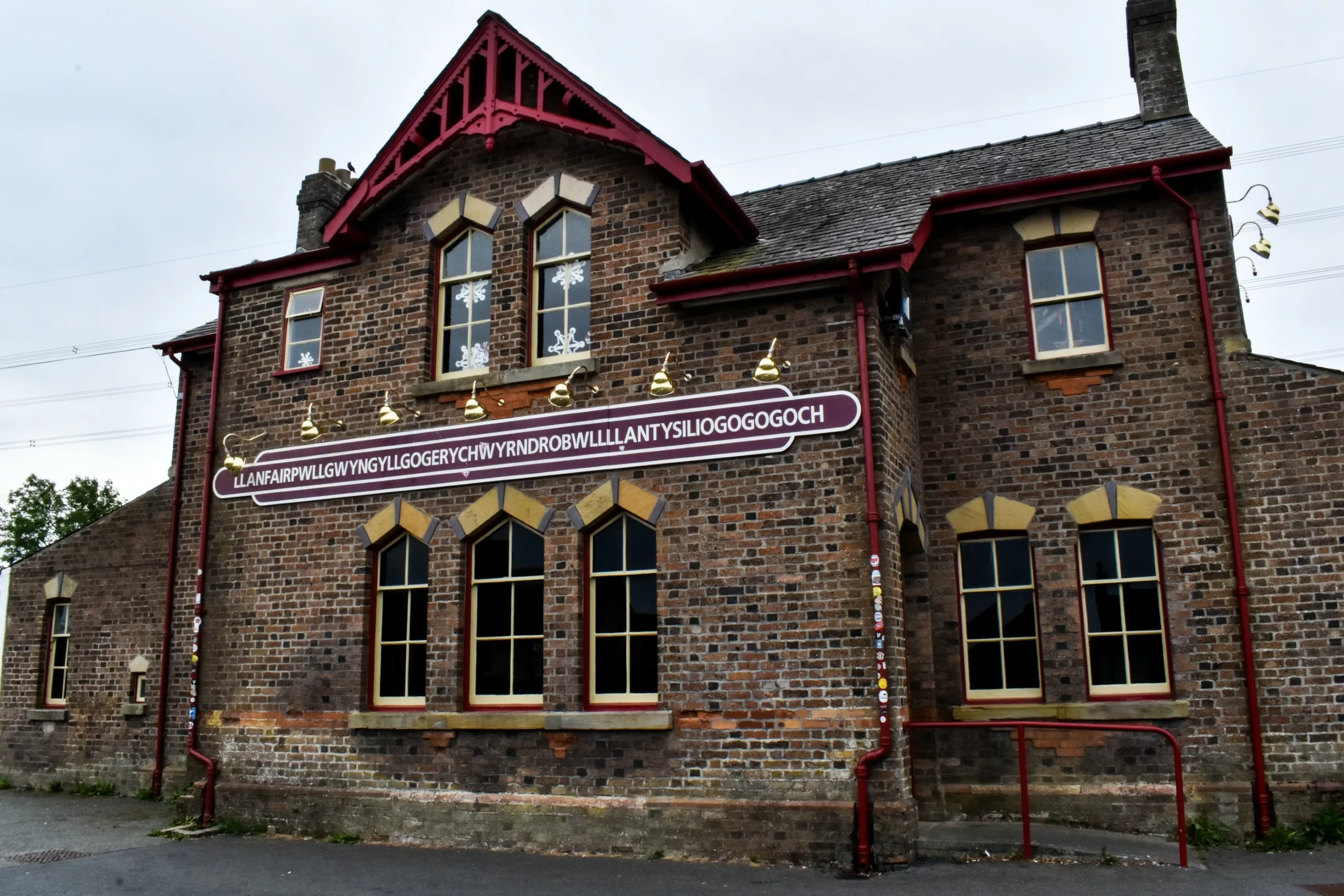 Le bâtiment en briques de la gare de Llanfairpwllgwyngyllgogerychwyrndrobwllllantysiliogogogoch, sur lequel figure un panneau indiquant le nom complet de la ville.