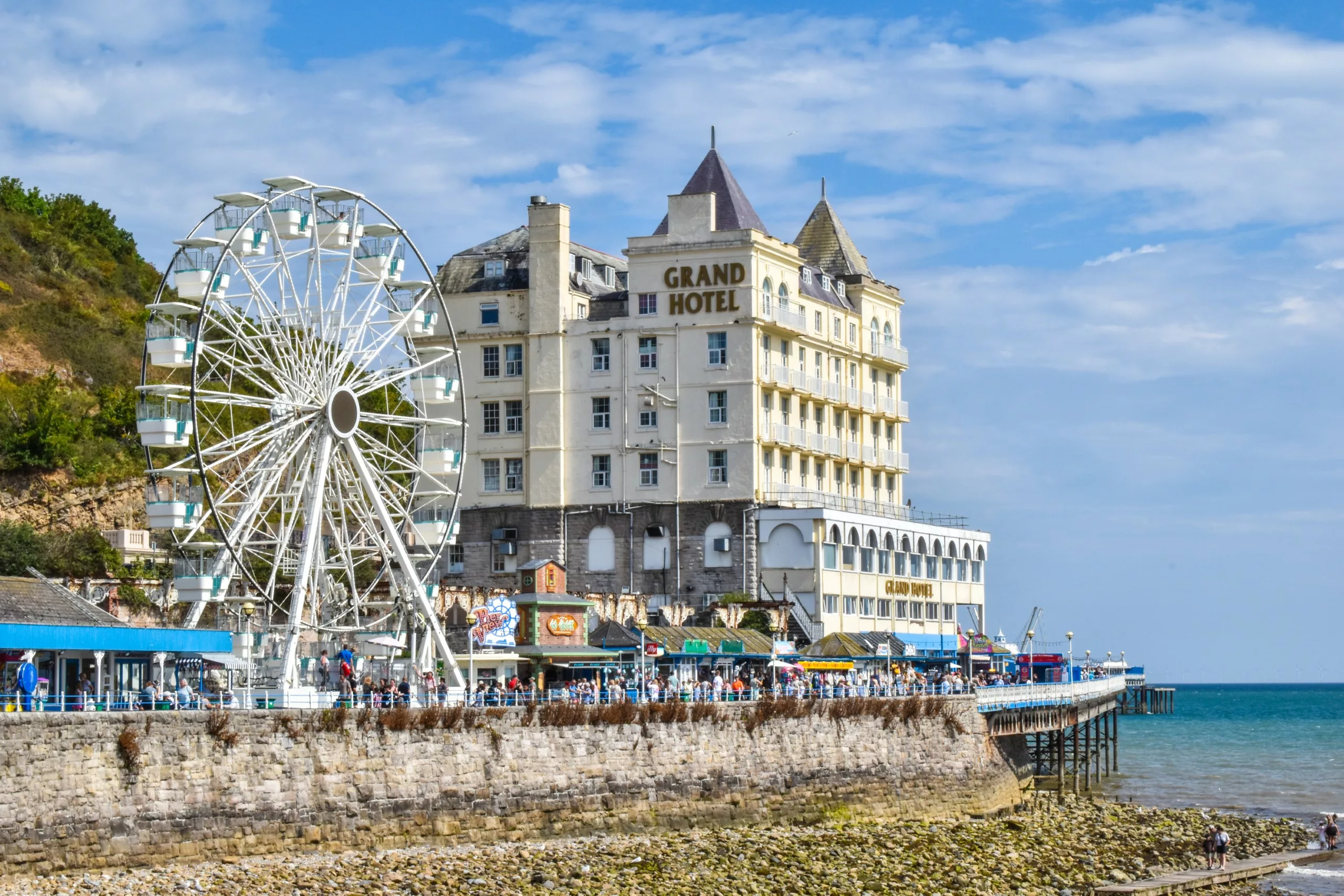 Le Grand Hôtel se dresse sur une falaise en bord de mer aà Llandudno, à côté d'une grande roue blanche qui surplombe une plage rocheuse.