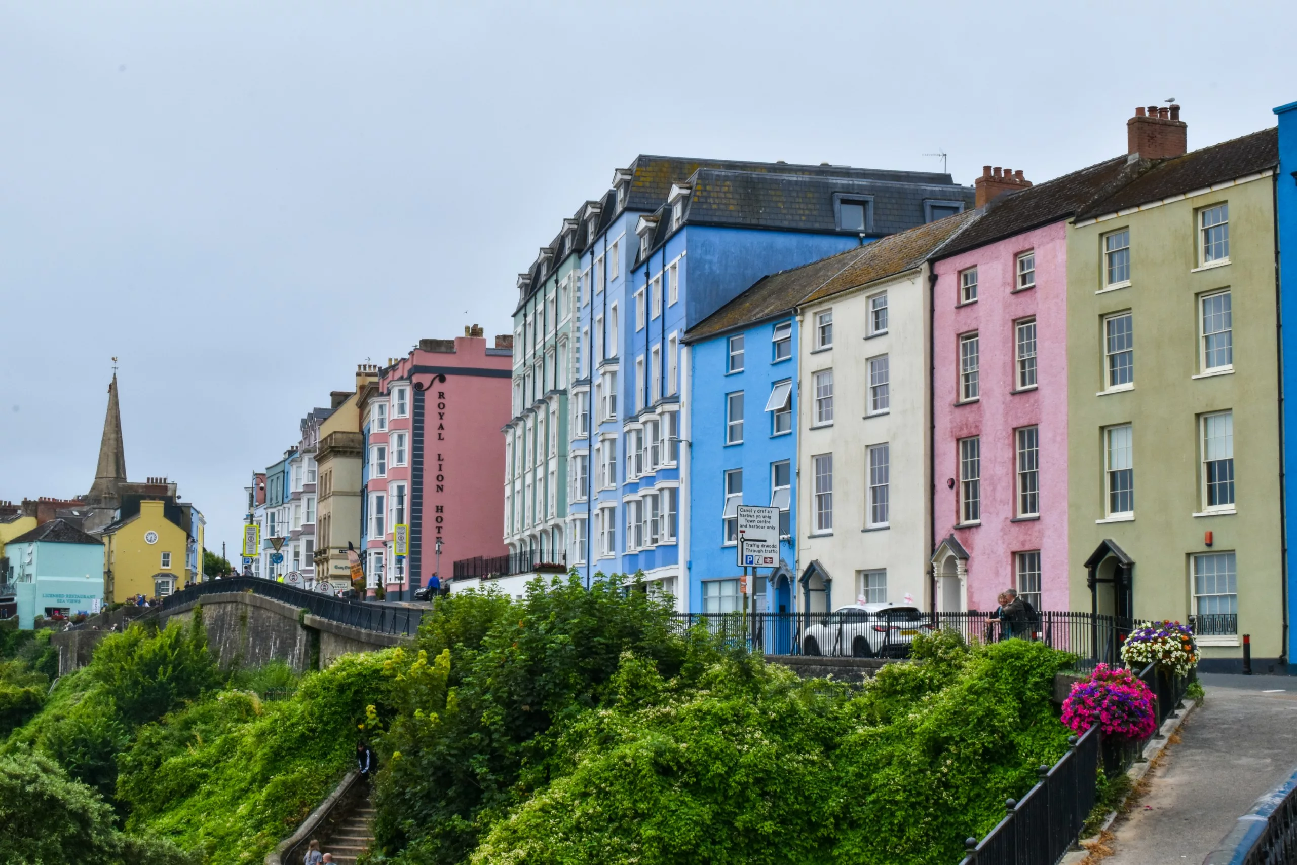 Une rangée de maisons mitoyennes colorées surplombant une falaise côtière et une végétation luxuriante : c'est la ville de Tenby à visiter au Pays de Galles.