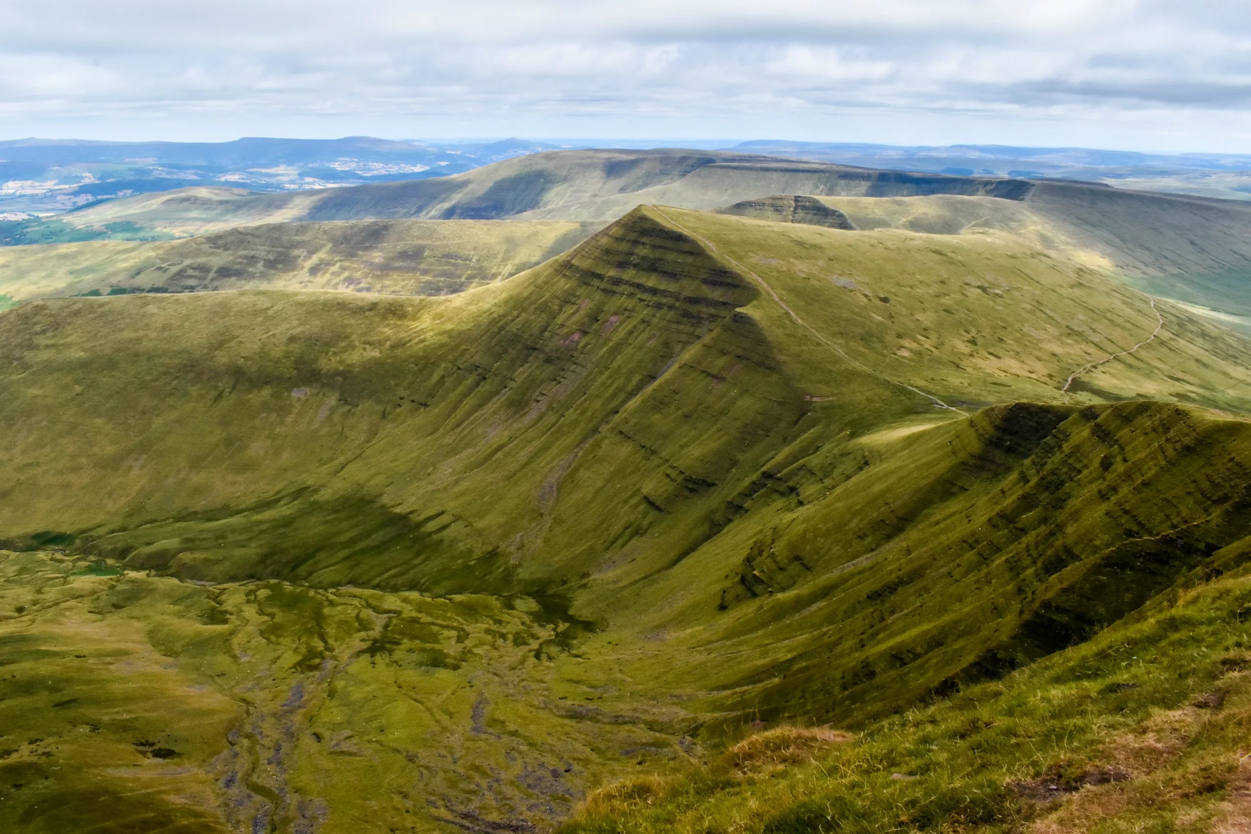 Un sentier de randonnée étroit serpente le long d'une crête verdoyante et en pente dans les Brecon Beacons, une destination très prisée à visiter au Pays de Galles.