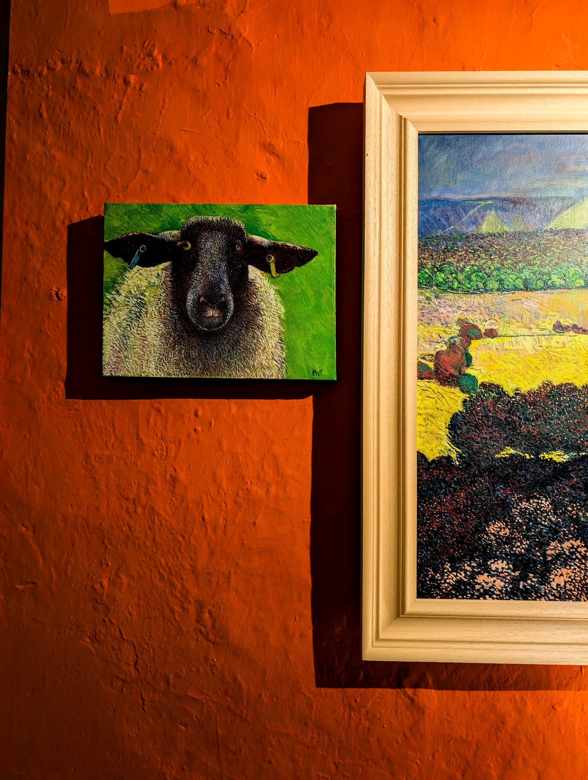 Intérieur d'un restaurant avec des murs rouges où sont accrochées des tableaux de peintures représentant un mouton et un paysage du Pays de Galles