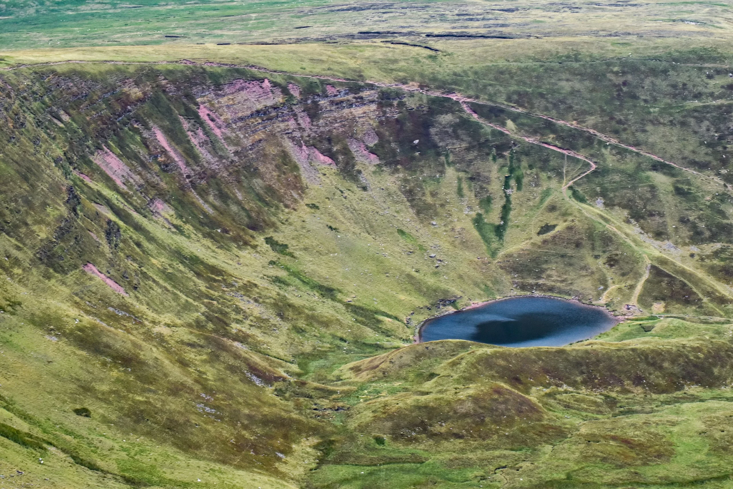 Au fond d'une vallée herbeuse profonde en forme de cuvette se trouve un petit lac sombre, entouré de pentes rocheuses escarpées.