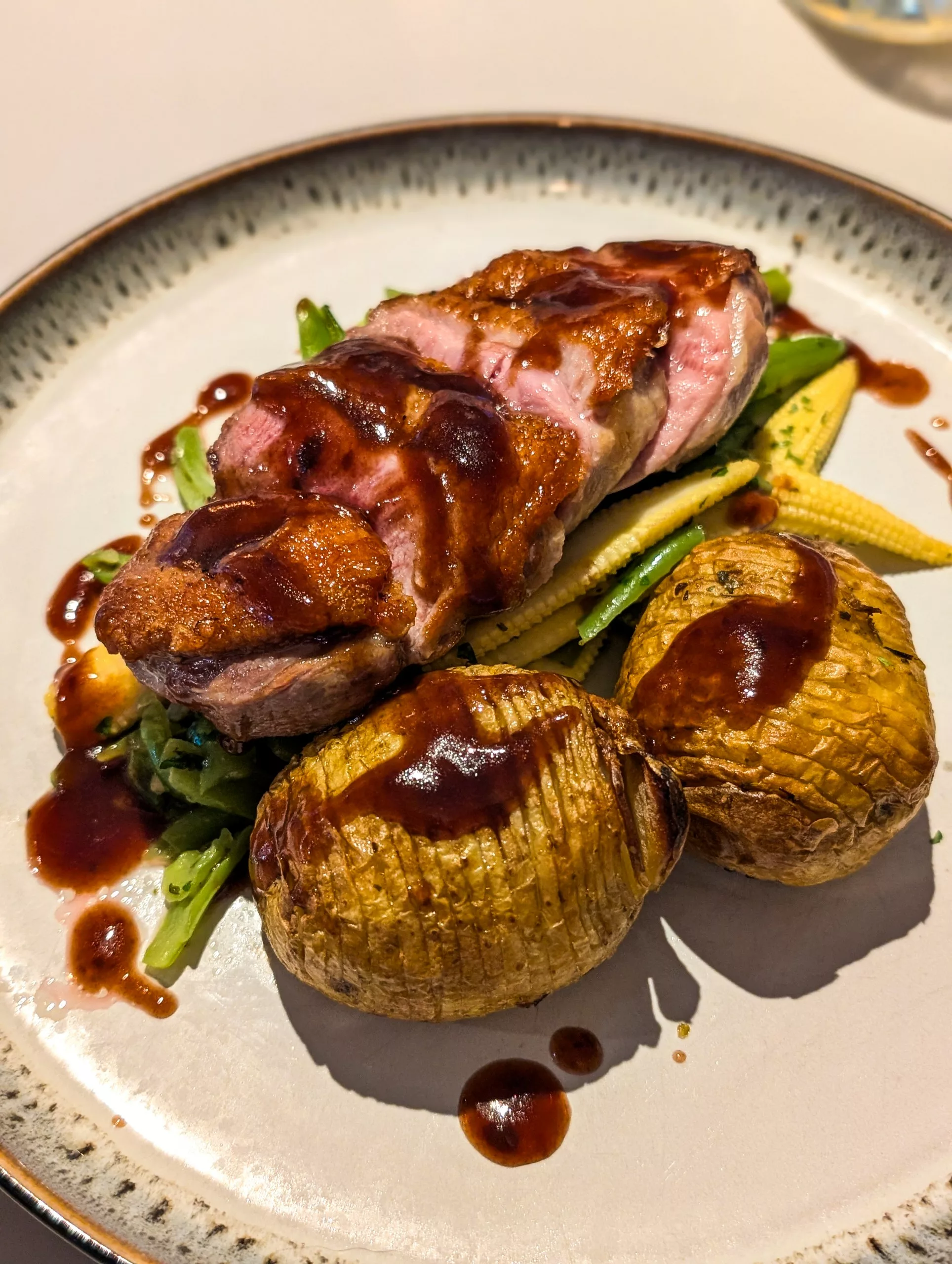 Une assiette blanche où se trouvent du magret de canard accompagné de pommes de terre et légumes, le tout recouvert d'un peu de sauce brune.