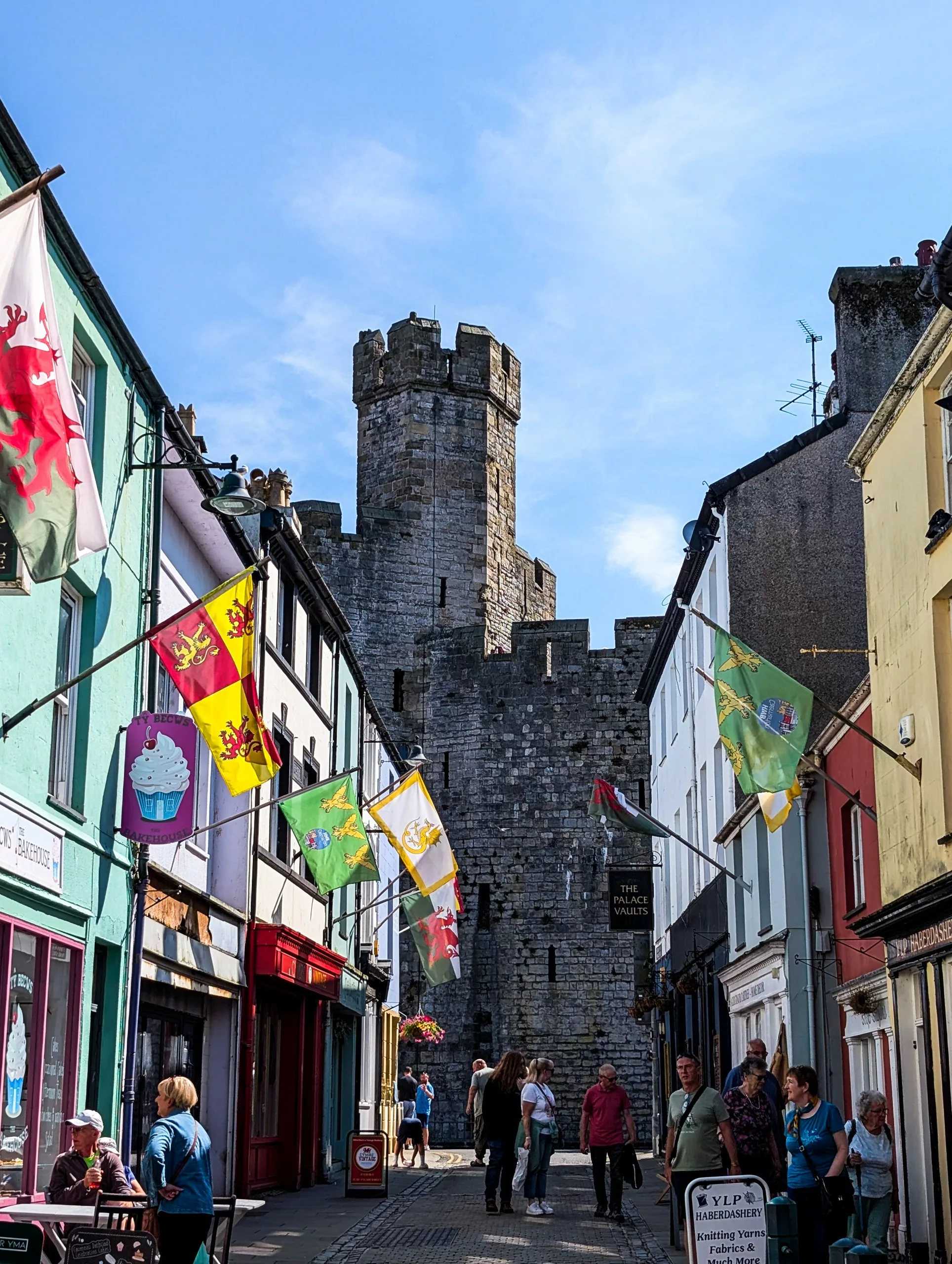 Une ruelle étroite de Caernarfon, bordée de boutiques et ornée de drapeaux, menant aux remparts médiévaux en pierre du château de la ville, un lieu incontournable à visiter au Pays de Galles.