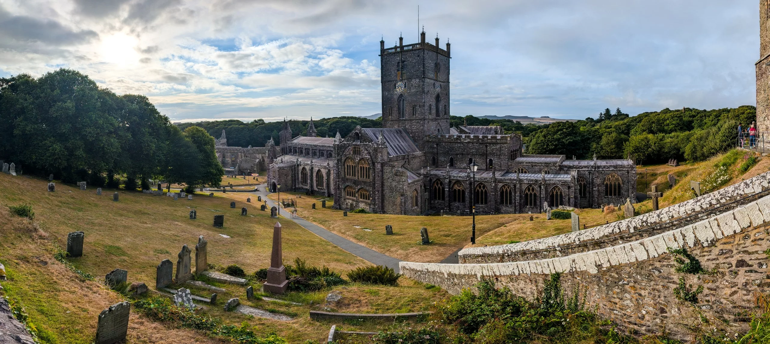Une grande cathédrale en pierre, dotée d'une tour horloge centrale, située dans un cimetière verdoyant parsemé de pierres tombales.