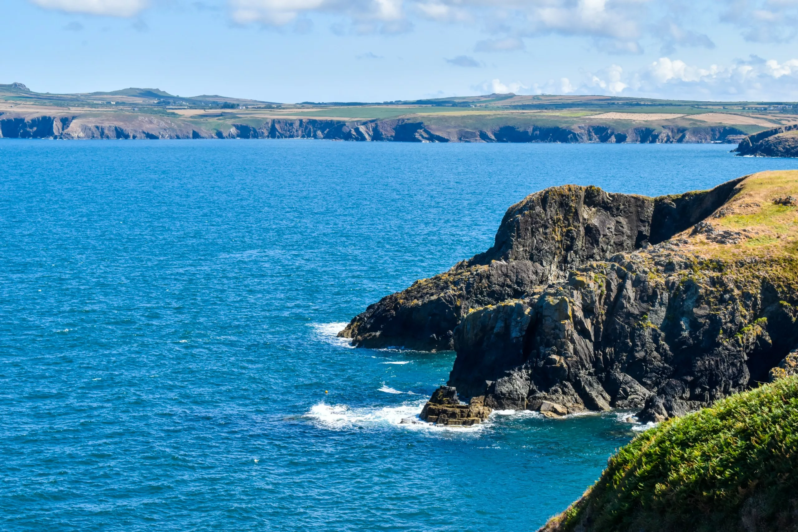Des falaises escarpées surplombant une baie d'un bleu profond, avec au loin un littoral sinueux au Pays de Galles.