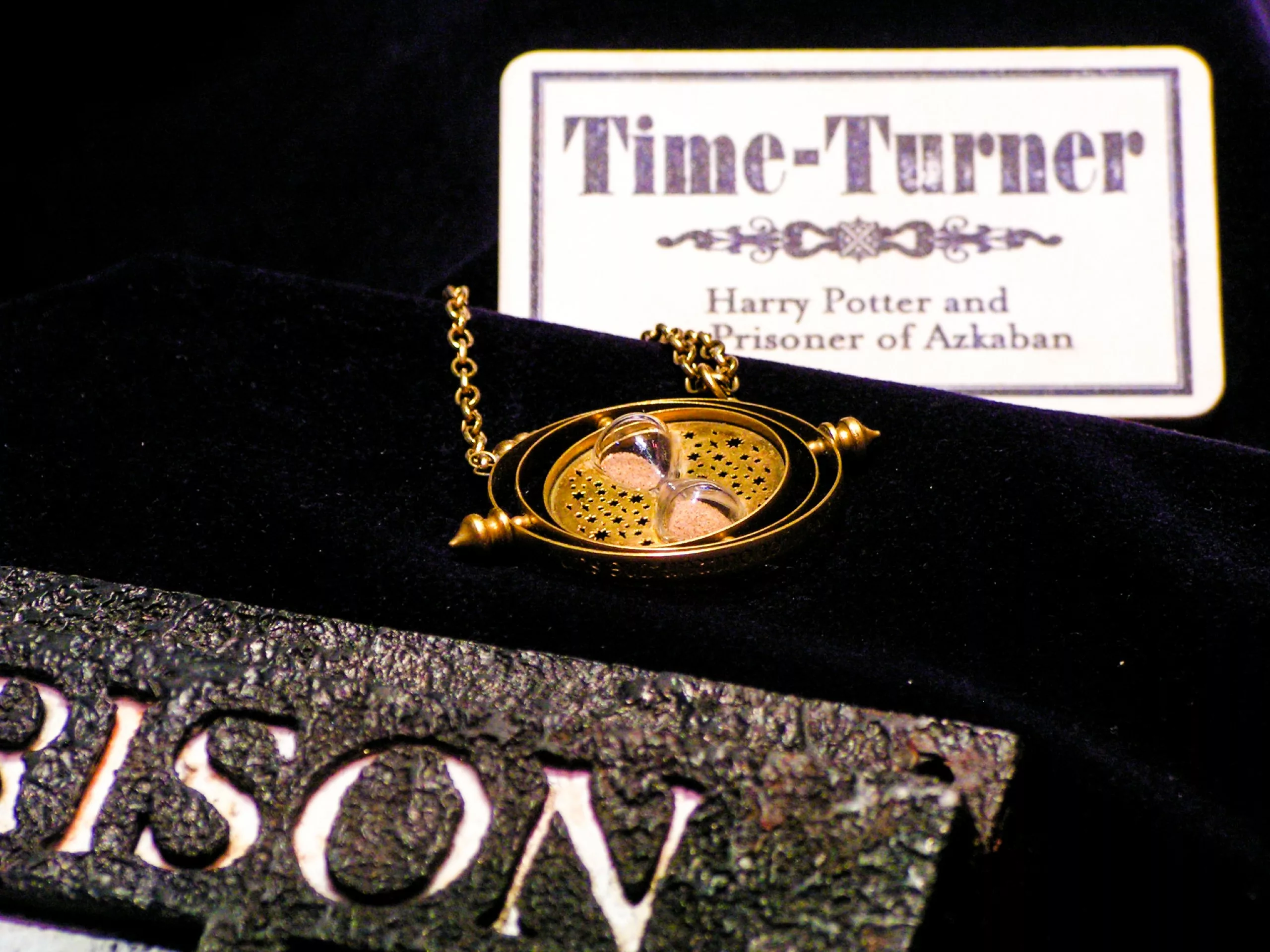 Le collier « Time-Turner » de Harry Potter, posé sur une surface en velours foncé, à côté d'une pancarte portant l'inscription « Time-Turner, Harry Potter et le Prisonnier d'Azkaban ».