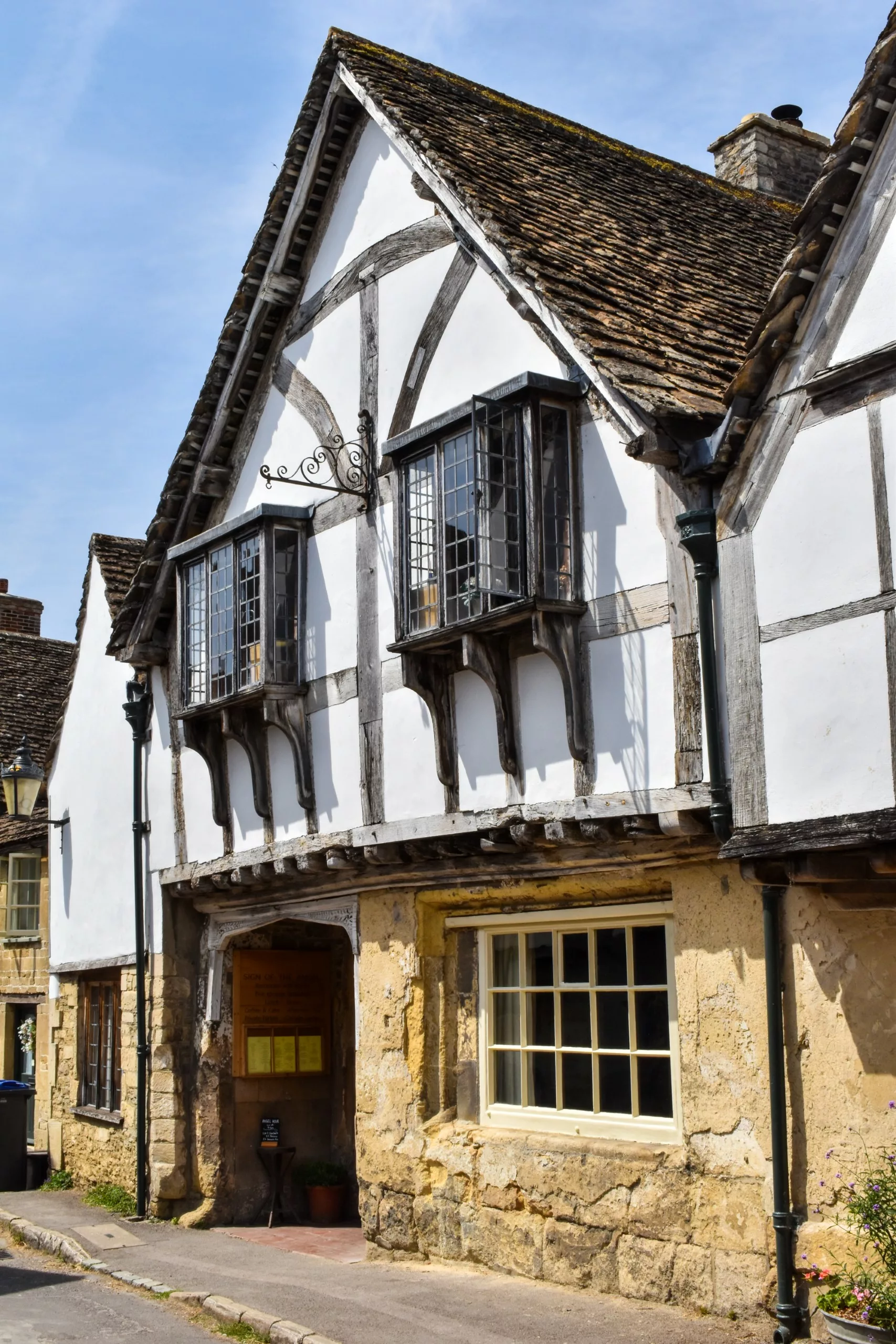 Une maison à colombages en Angleterre, vue dans les films Harry Potter, dotée de baies vitrées en saillie et d'un rez-de-chaussée en pierre.